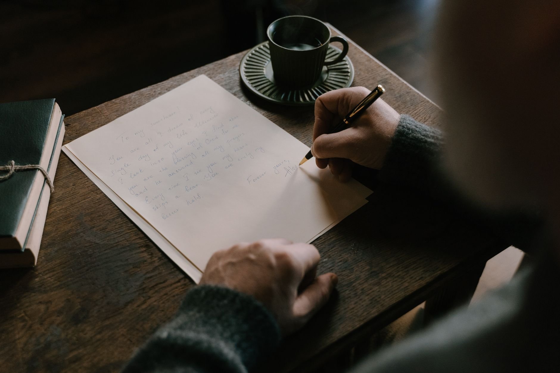 An adult writing at a warm wooden desk with coffee nearby